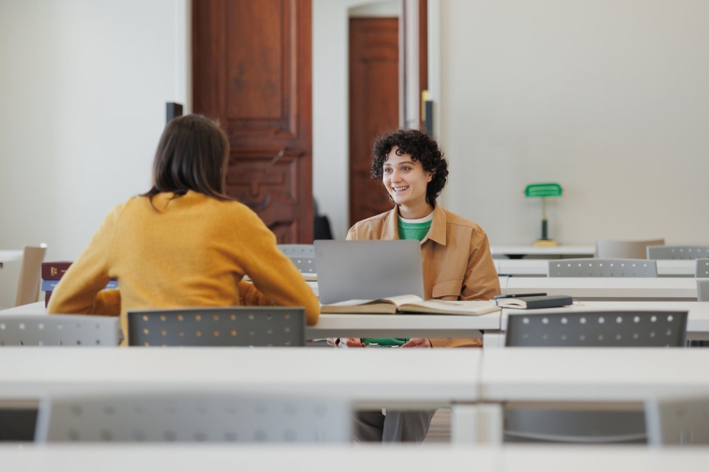 Two women are smiling and working on laptops.