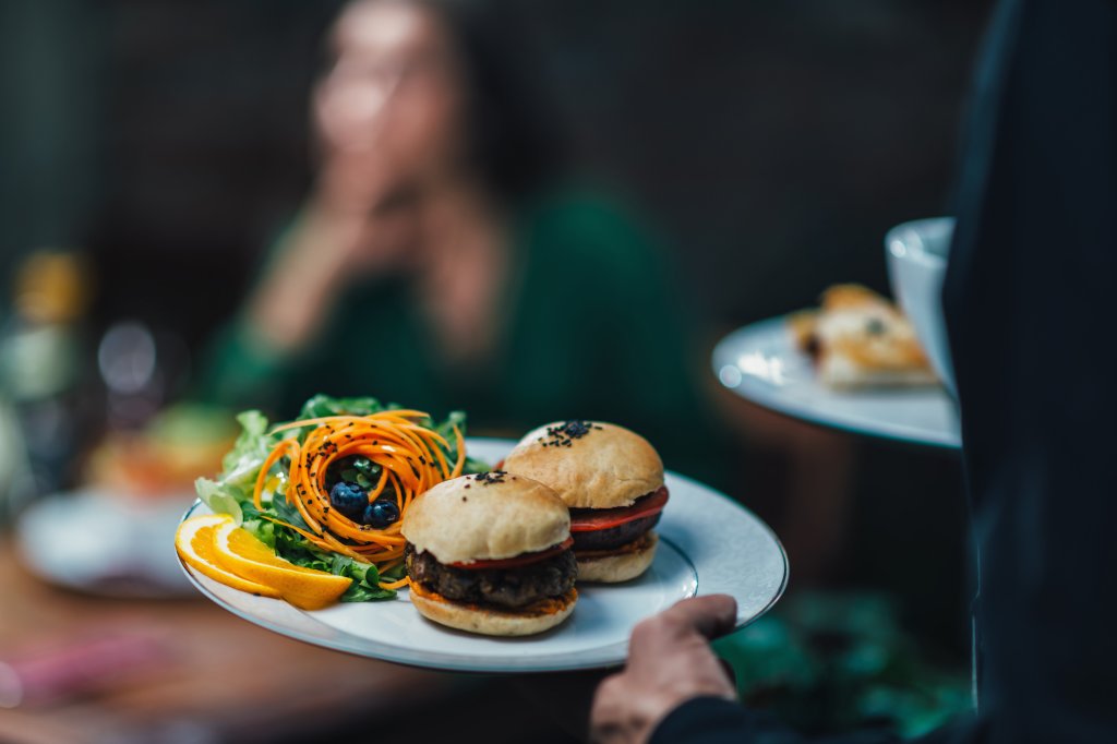 A waiter is carrying out a meal of 2 small vegan burgers and salad.