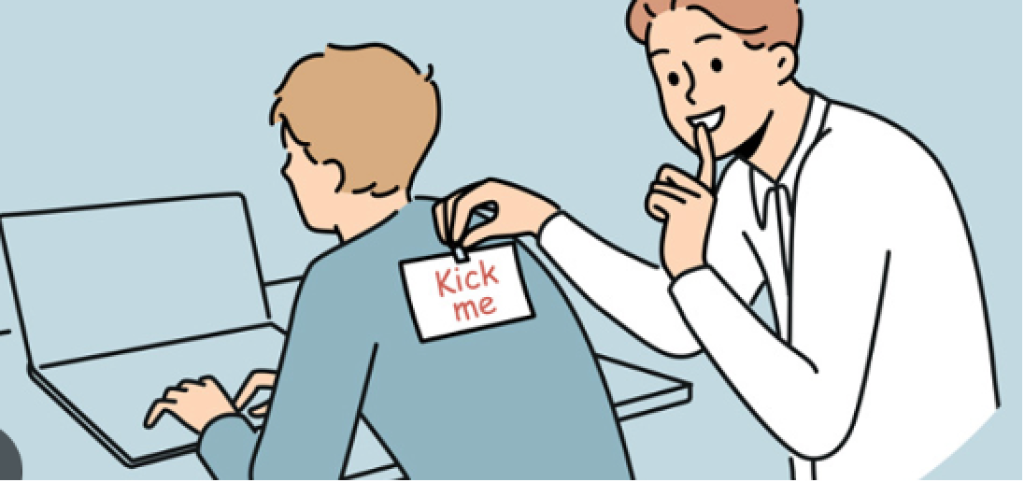 A man is putting a kick me sign on his colleague's back.