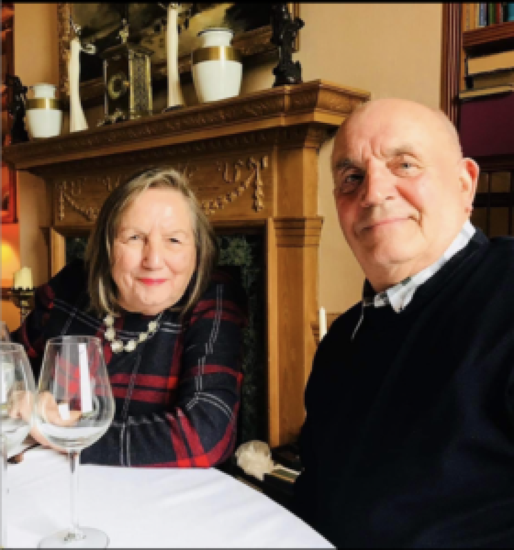 An older woman and man are sat at a table with 2 wine glasses.
