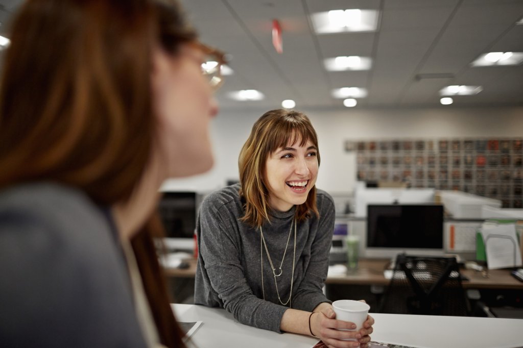 Two women are seated in an office, talking.