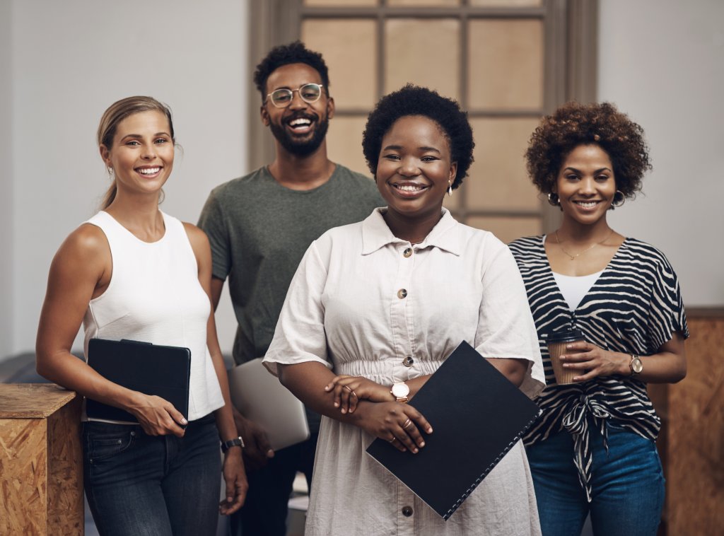 4 people are standing together smiling as they wait to be interviewed for a job role.