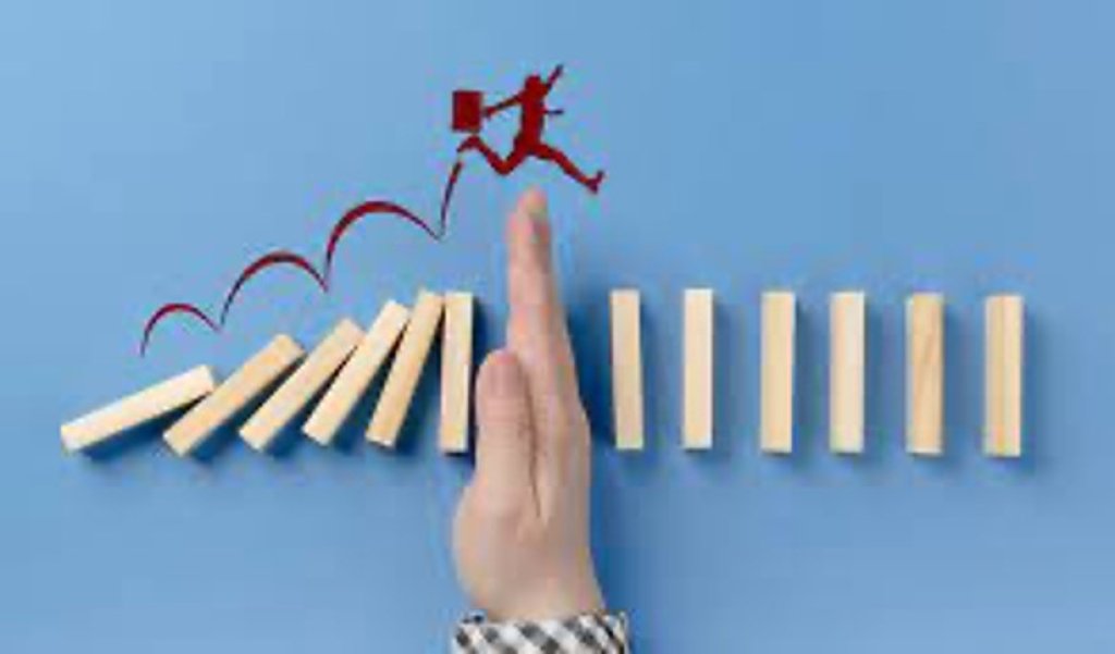 A man has his hand placed halfway between fallen blocks and standing blocks. Above his hand is a drawing of a man with a briefcase leaping to the standing blocks.