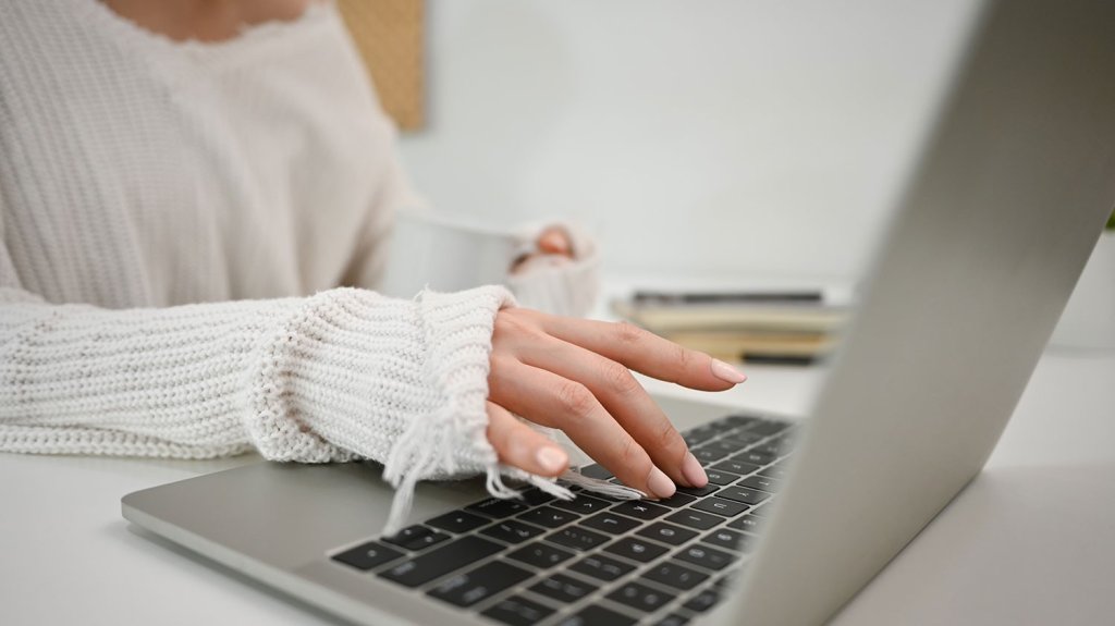 A lady with freshly painted nails is typing on a laptop.
