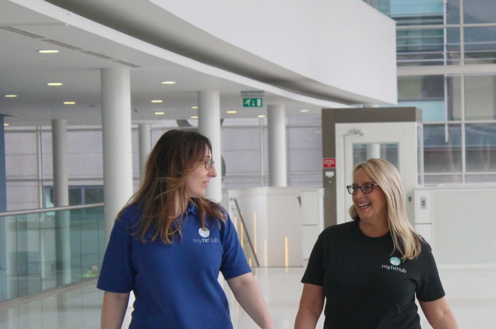 An HR team are walking through a corporate workspace. They are looking at each other an smiling.