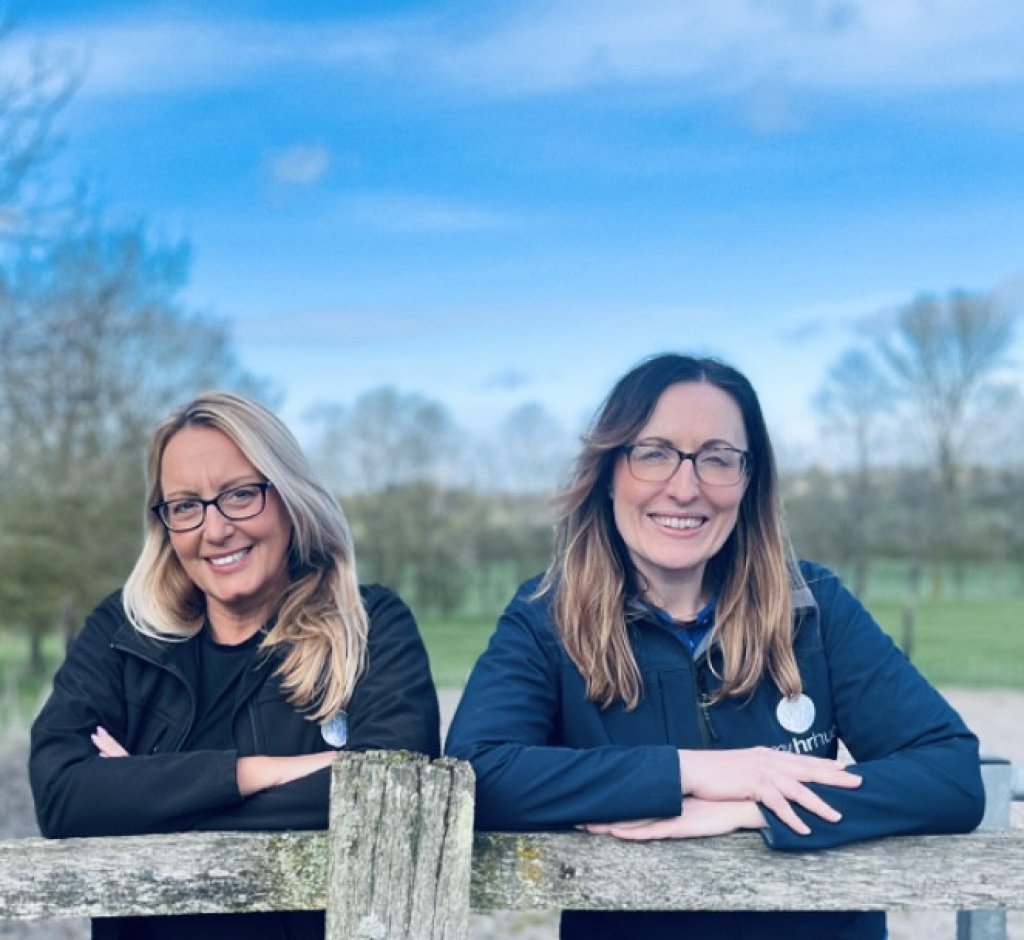 An HR team are leaning on a wooden fence. There are trees and fields in the background.